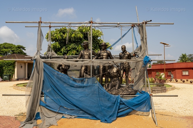 Place des Enchères Ouidah ; Place Chacha slave market Benin ; bronze sculptures slave trade ; spheres ground memorial Ouidah ; monumental heads Xweda Fon Yoruba ; memorial public art West Africa ; night lighting Ouidah square ; red laterite ground ; de Souza house Singbomey ; Afro-Brazilian heritage Ouidah ; Benin Revealed program