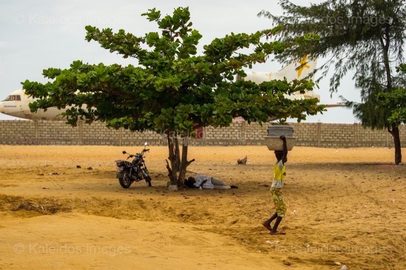 Barakah, L1011 TriStar, Lockheed L1011, abandoned TriStar, aircraft wreck, grounded aircraft, white fuselage, derelict cockpit, empty cabin, Cotonou beach, Cadjéhoun beach, Cotonou Benin, West Africa, Benin airport, Atlantic coastline, coastal Benin, corroded wreck, marine rust, deterioration, salt corrosion, decay, abandonment, dereliction, dilapidation, environmental erosion, aviation heritage, industrial archaeology, failed tourism project, open-air museum, urban art, colonial relic, Benin history, alternative tourism, architectural curiosity, aviation history, hajj pilgrimage, Air Rum airline, defunct carrier, humanitarian transport, international migration, historical traces, industrial heritage, stranded aircraft, tourist attraction, urban exploration, ruin photography, beach adventure, Beninese leisure, amusement park, immersive experience, urban safari, overcast sky, sunset beach, tropical storm, coastal erosion, sea salt, Atlantic Ocean, white sand, coastal vegetation, gleaming white, nature-machine contrast, aerospace geometry, outstretched wings, empty windows, cabin stairway, cockpit instruments, time displacement, obsolescence, suspended time, liminality, aborted transformation, urban memory, unfinished dream, nature-industry symbiosis, tourism ghost, frozen history