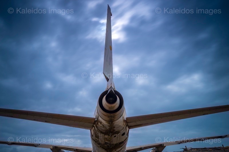 Barakah, L1011 TriStar, Lockheed L1011, abandoned TriStar, aircraft wreck, grounded aircraft, white fuselage, derelict cockpit, empty cabin, Cotonou beach, Cadjéhoun beach, Cotonou Benin, West Africa, Benin airport, Atlantic coastline, coastal Benin, corroded wreck, marine rust, deterioration, salt corrosion, decay, abandonment, dereliction, dilapidation, environmental erosion, aviation heritage, industrial archaeology, failed tourism project, open-air museum, urban art, colonial relic, Benin history, alternative tourism, architectural curiosity, aviation history, hajj pilgrimage, Air Rum airline, defunct carrier, humanitarian transport, international migration, historical traces, industrial heritage, stranded aircraft, tourist attraction, urban exploration, ruin photography, beach adventure, Beninese leisure, amusement park, immersive experience, urban safari, overcast sky, sunset beach, tropical storm, coastal erosion, sea salt, Atlantic Ocean, white sand, coastal vegetation, gleaming white, nature-machine contrast, aerospace geometry, outstretched wings, empty windows, cabin stairway, cockpit instruments, time displacement, obsolescence, suspended time, liminality, aborted transformation, urban memory, unfinished dream, nature-industry symbiosis, tourism ghost, frozen history
