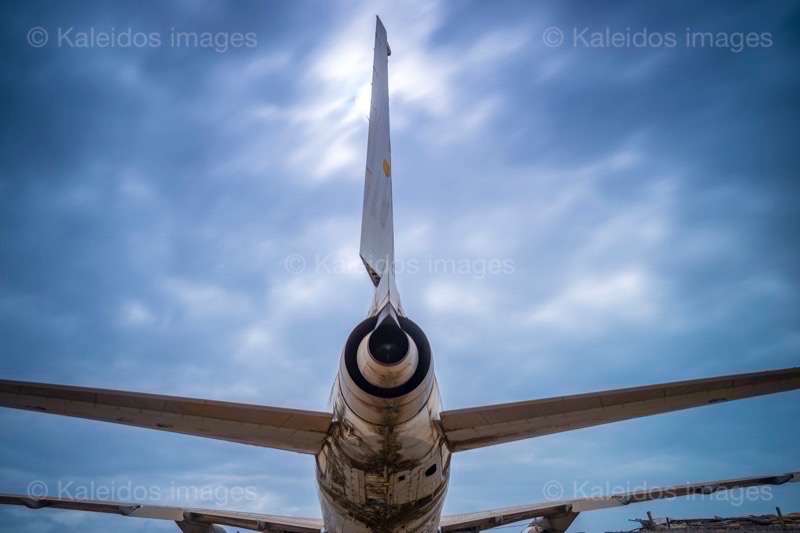 Barakah, L1011 TriStar, Lockheed L1011, abandoned TriStar, aircraft wreck, grounded aircraft, white fuselage, derelict cockpit, empty cabin, Cotonou beach, Cadjéhoun beach, Cotonou Benin, West Africa, Benin airport, Atlantic coastline, coastal Benin, corroded wreck, marine rust, deterioration, salt corrosion, decay, abandonment, dereliction, dilapidation, environmental erosion, aviation heritage, industrial archaeology, failed tourism project, open-air museum, urban art, colonial relic, Benin history, alternative tourism, architectural curiosity, aviation history, hajj pilgrimage, Air Rum airline, defunct carrier, humanitarian transport, international migration, historical traces, industrial heritage, stranded aircraft, tourist attraction, urban exploration, ruin photography, beach adventure, Beninese leisure, amusement park, immersive experience, urban safari, overcast sky, sunset beach, tropical storm, coastal erosion, sea salt, Atlantic Ocean, white sand, coastal vegetation, gleaming white, nature-machine contrast, aerospace geometry, outstretched wings, empty windows, cabin stairway, cockpit instruments, time displacement, obsolescence, suspended time, liminality, aborted transformation, urban memory, unfinished dream, nature-industry symbiosis, tourism ghost, frozen history