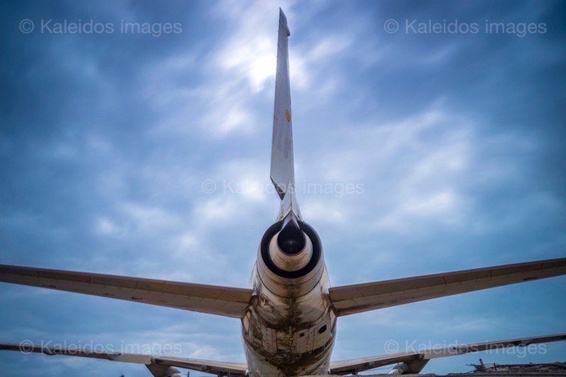 Barakah, L1011 TriStar, Lockheed L1011, abandoned TriStar, aircraft wreck, grounded aircraft, white fuselage, derelict cockpit, empty cabin, Cotonou beach, Cadjéhoun beach, Cotonou Benin, West Africa, Benin airport, Atlantic coastline, coastal Benin, corroded wreck, marine rust, deterioration, salt corrosion, decay, abandonment, dereliction, dilapidation, environmental erosion, aviation heritage, industrial archaeology, failed tourism project, open-air museum, urban art, colonial relic, Benin history, alternative tourism, architectural curiosity, aviation history, hajj pilgrimage, Air Rum airline, defunct carrier, humanitarian transport, international migration, historical traces, industrial heritage, stranded aircraft, tourist attraction, urban exploration, ruin photography, beach adventure, Beninese leisure, amusement park, immersive experience, urban safari, overcast sky, sunset beach, tropical storm, coastal erosion, sea salt, Atlantic Ocean, white sand, coastal vegetation, gleaming white, nature-machine contrast, aerospace geometry, outstretched wings, empty windows, cabin stairway, cockpit instruments, time displacement, obsolescence, suspended time, liminality, aborted transformation, urban memory, unfinished dream, nature-industry symbiosis, tourism ghost, frozen history